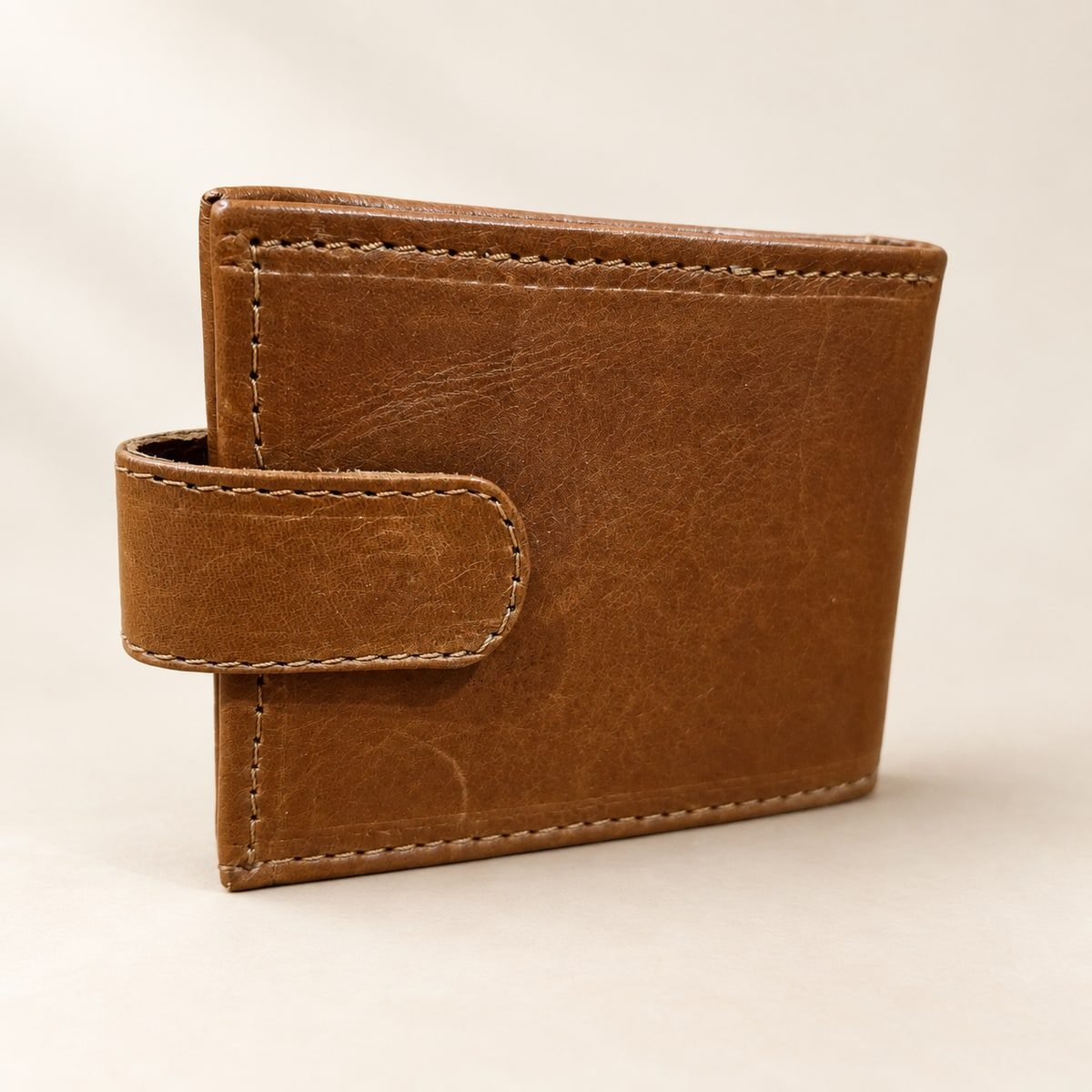 Brown leather bifold wallet with a stitched closure tab on a warm cream background.