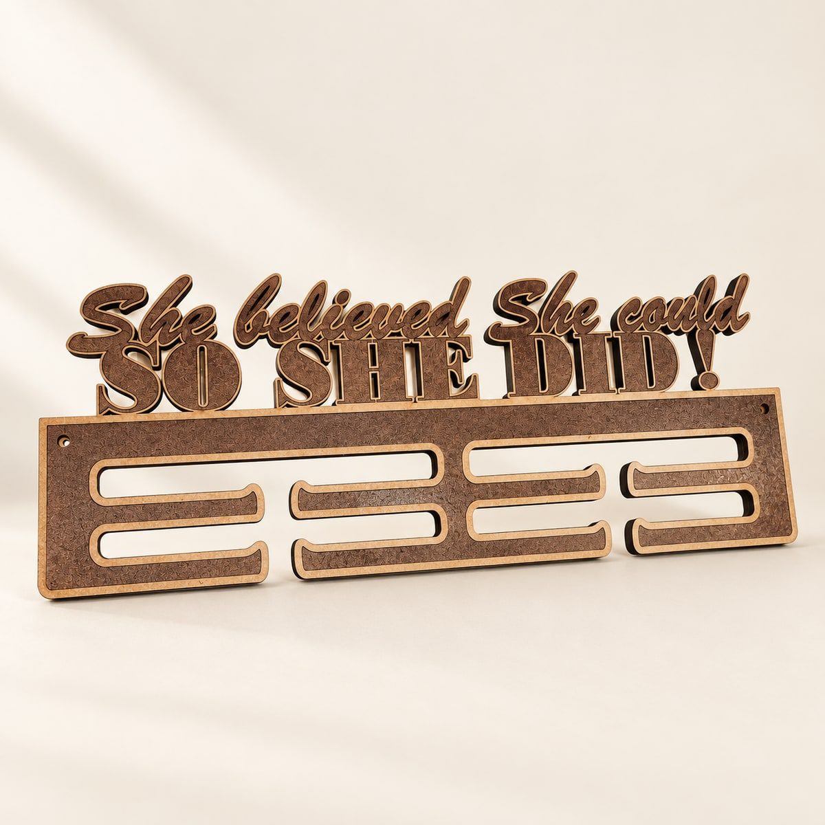Wooden medal display reading She believed She could, So She Did, with slots beneath the lettering.