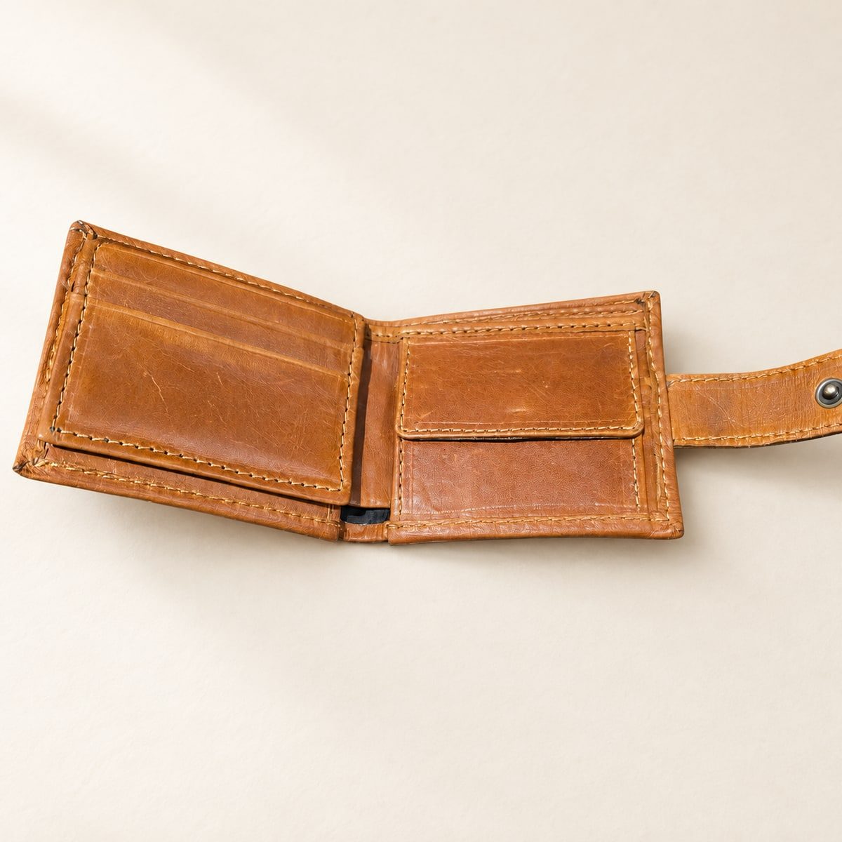 Open tan leather wallet showing card pockets, a flap pocket, stitching and a closure tab.