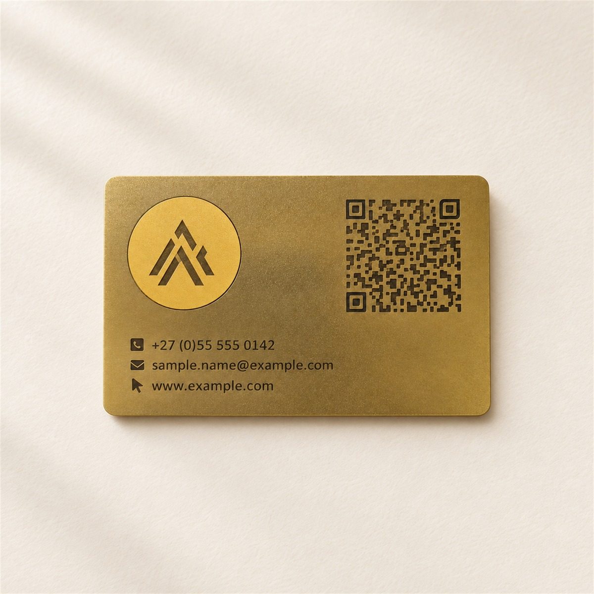 Brushed gold metal business card engraved with a monogram, a QR code and three lines of sample contact details.